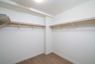 A spacious walk-in closet in a modern apartment featuring minimalist white shelving, wooden hanging rods, and light wood-plank flooring.