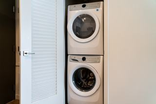 A modern laundry closet featuring stacked, white Electrolux front-loading washer and dryer units behind a white slatted door.