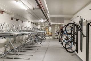 A modern, well-lit, secure indoor bike storage room featuring rows of sleek black vertical and horizontal wall-mounted racks holding several bicycles securely.