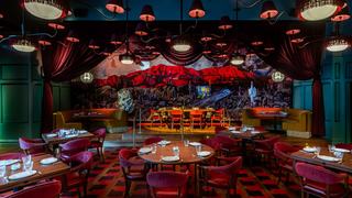 The "Theater Room" at El Presidente DC, featuring a dramatic 33-foot desert mountainscape mural by Annelisa Leinbach. The room is designed with deep scarlet velvet seating, dark red drapes, and a tiered layout that creates a cinematic, "more-is-more" atmosphere inspired by Mexico City.