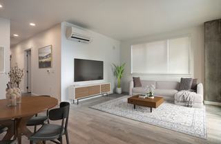 A bright, modern apartment living room with hardwood-style flooring and a sleek, wall-mounted air conditioning unit above a large window overlooking the Seattle skyline.