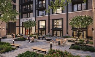 serene street-level courtyard at The Victor apartments, featuring modern wood-slat benches, lush concrete planters, and large windows overlooking the landscaped entryway.