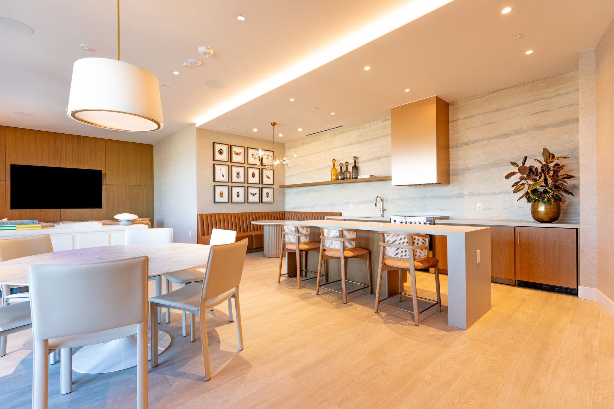 Modern catering kitchen and lounge featuring a copper range hood, tan leather banquette, and a marble dining table with a view toward the outdoor terrace.