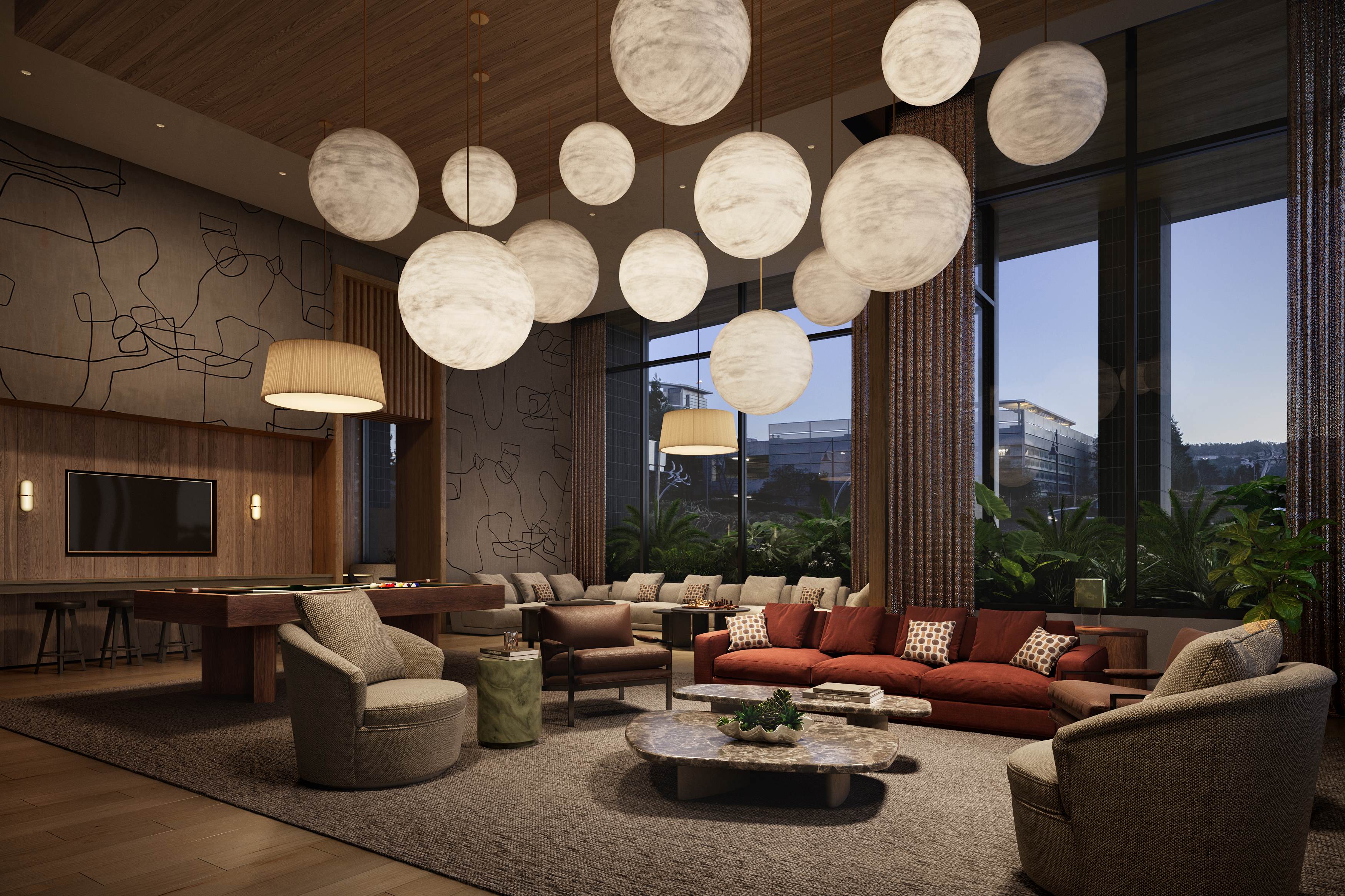A wide-angle interior view of the Revery club lounge featuring double-height ceilings and a sophisticated modern design. The room is illuminated by a cluster of large, glowing spherical pendant lights. The space includes a red velvet sofa, marble coffee tables, mid-century modern armchairs, a wooden billiards table, and large windows looking out onto lush outdoor landscaping at evening.