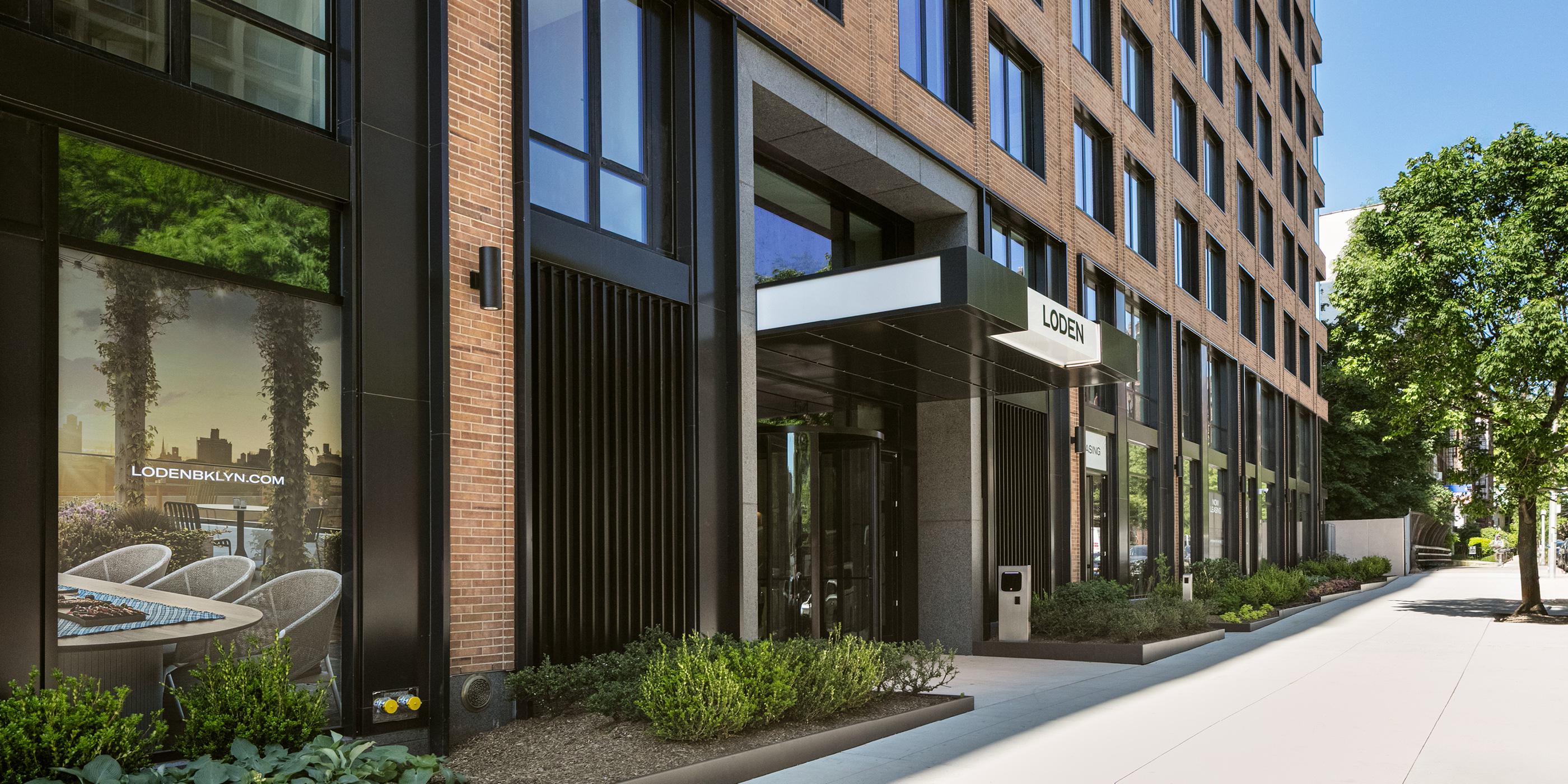 exterior and entrance of the new loden apartment building, showcasing attractive modern design and large windows, trees planted on the surrounding sidewalks, ground-floor retail, and understated design profile that fits in with the surrounding neighborhood. 