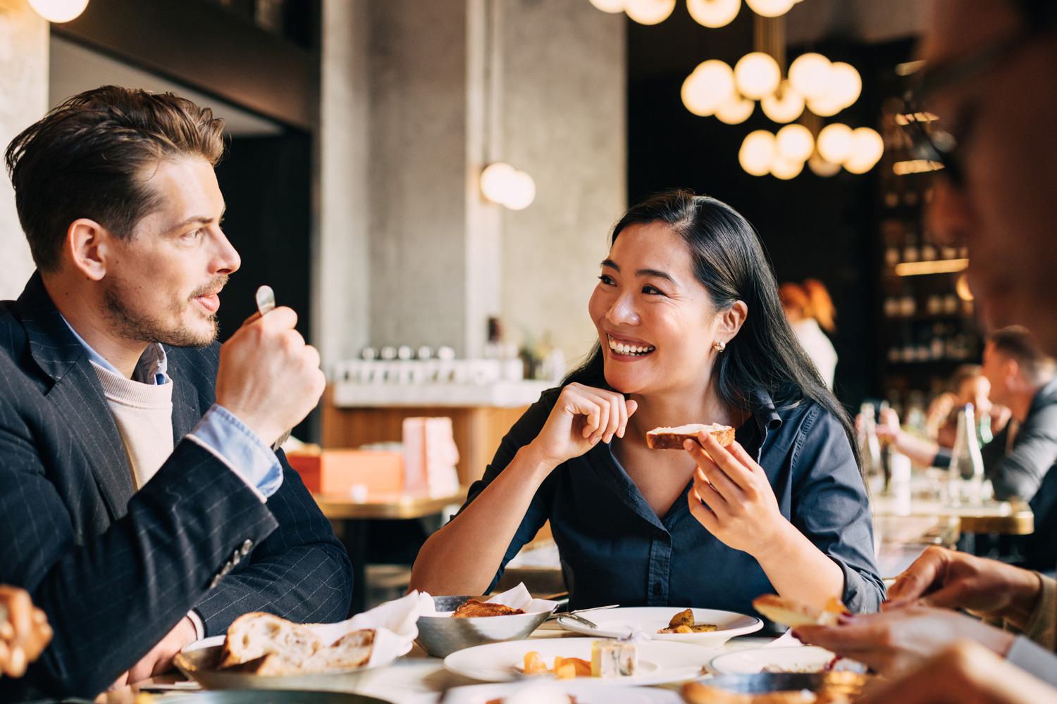 A man and a smiling woman sharing bread and conversation during a meal at a stylish, upscale restaurant.