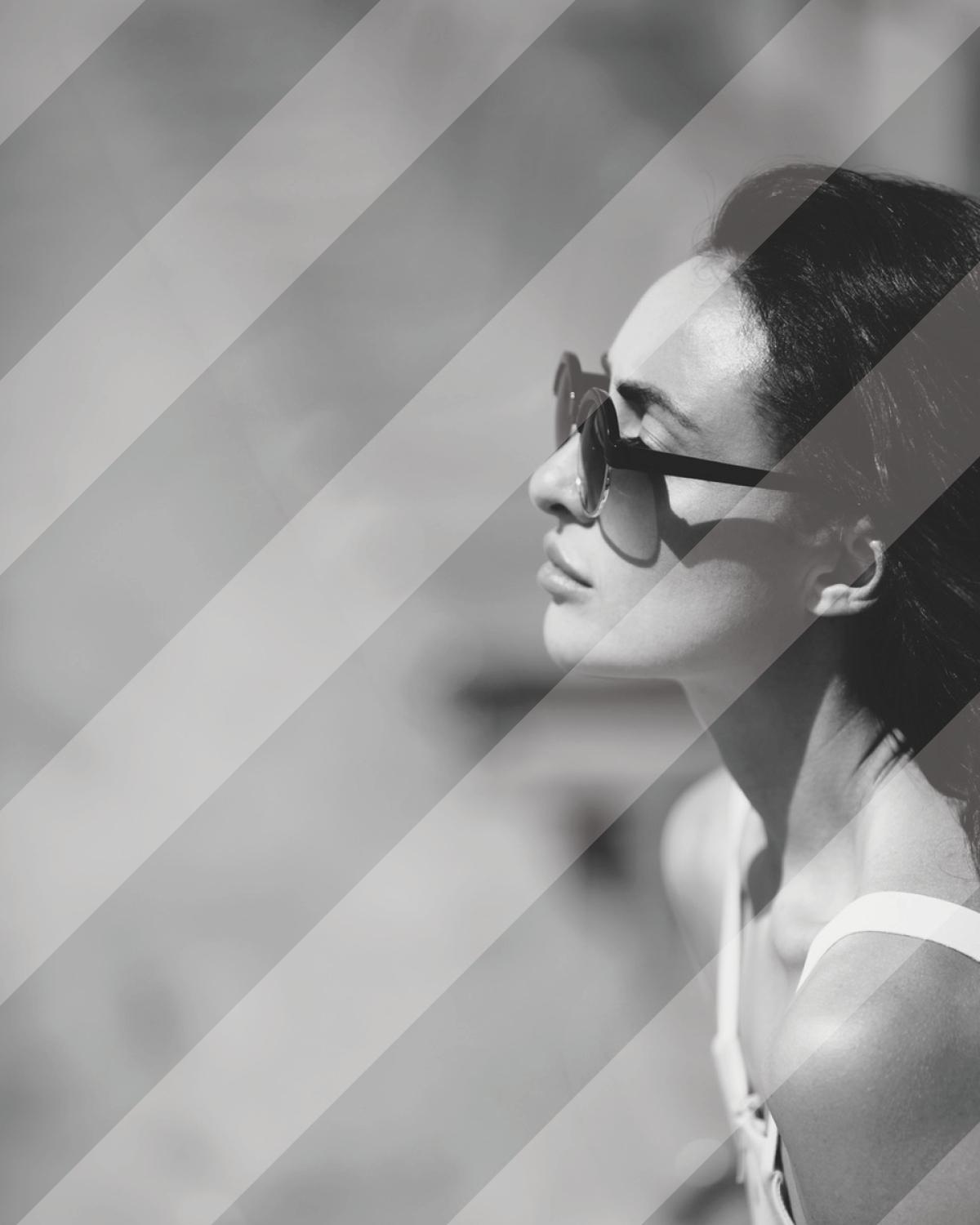 Black and white portrait of a woman in profile wearing dark sunglasses and a top with white straps.