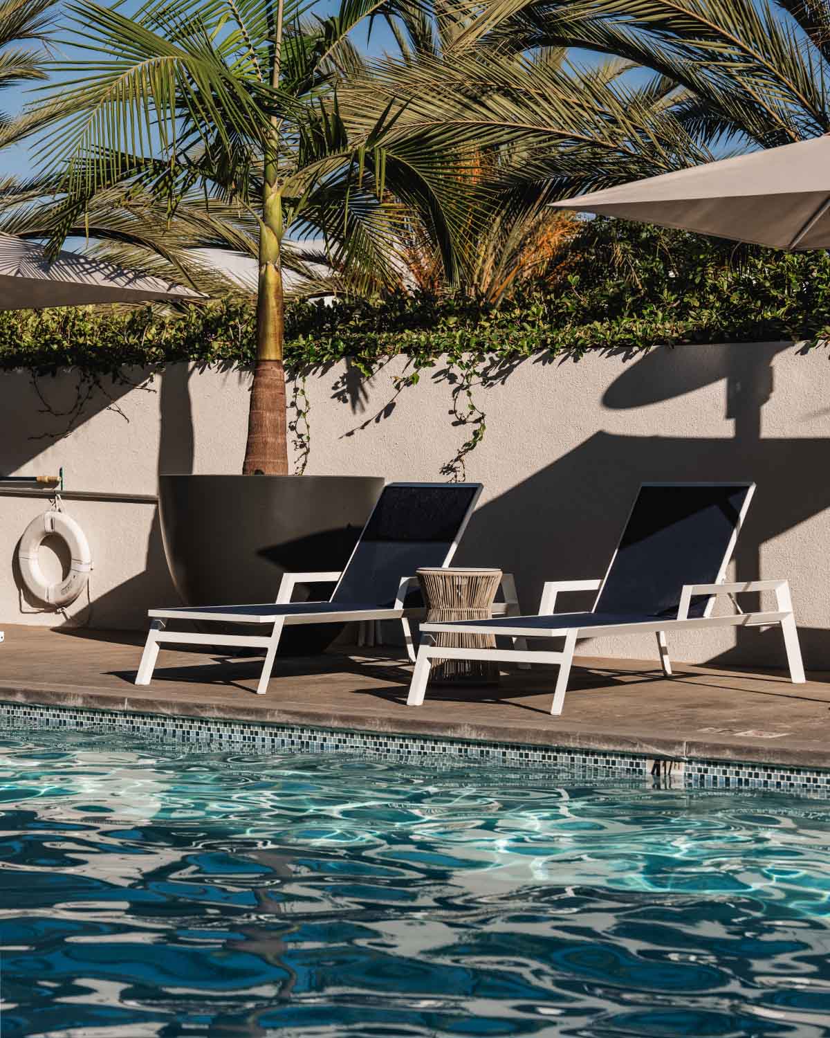 Modern indoor resident lounge featuring plush seating, a large TV console, woven pendant lights, and glass doors opening to an outdoor patio with a fire pit.