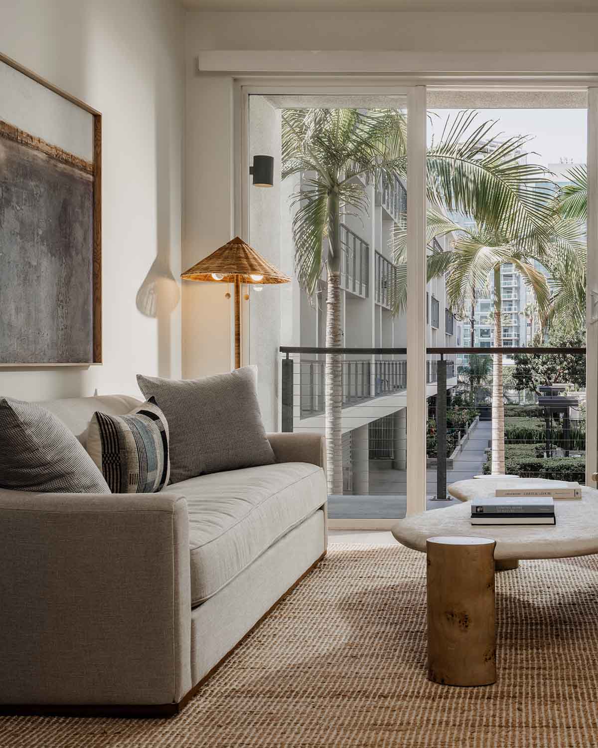 Sunlit townhome living area with low-profile beige seating, round marble coffee table, and a potted olive tree.