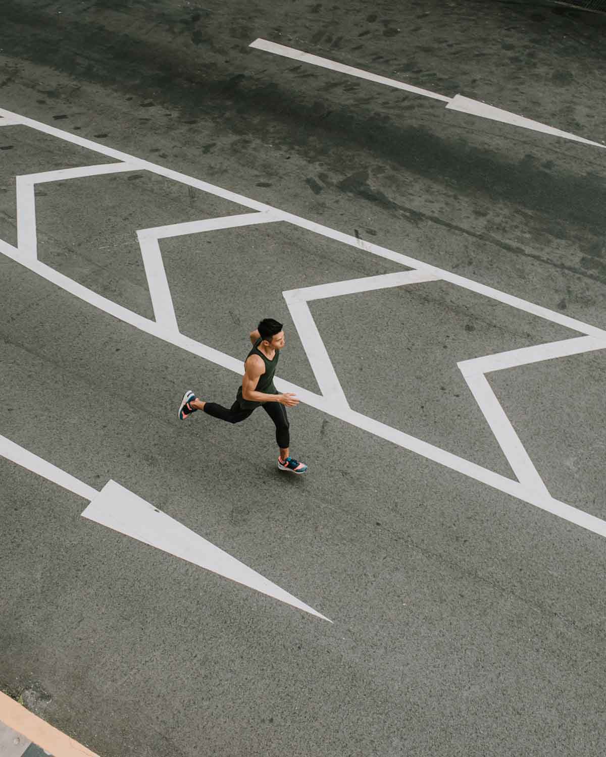 Aerial view of a man jogging along a paved road with white chevron directional arrows.