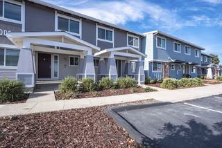 A row of modern grey and blue townhomes at Admirals Cove featuring covered front porches and paved parking spaces directly in front of the home entrances.