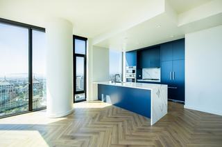 A luxury Atlas penthouse interior showcasing a marble waterfall kitchen island with an integrated wine fridge, herringbone wood floors, and massive windows overlooking the San Francisco Bay.