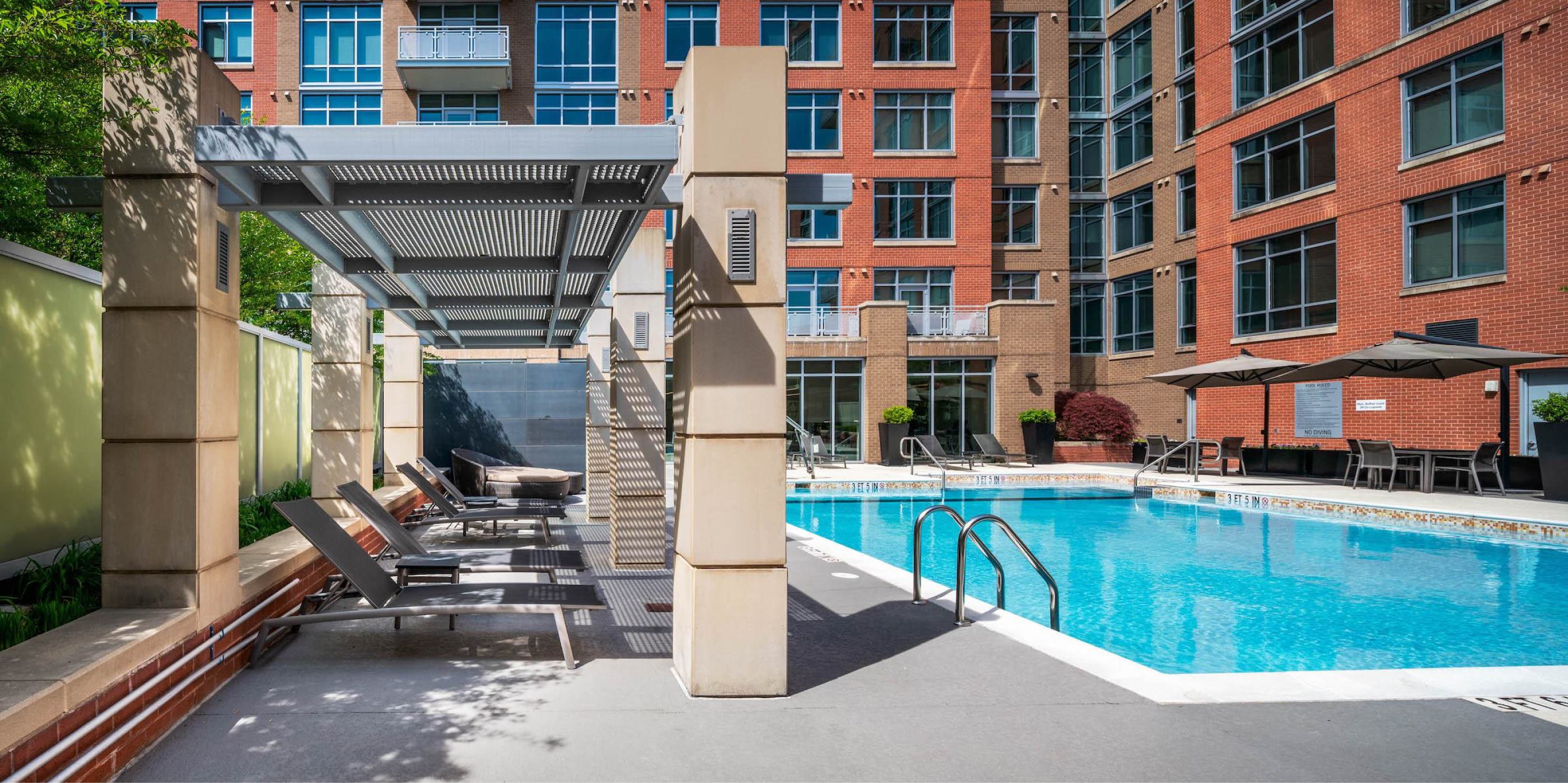 Outdoor swimming pool courtyard at Avant Reston with lounge chairs under a pergola, patio seating, and brick apartment facade.