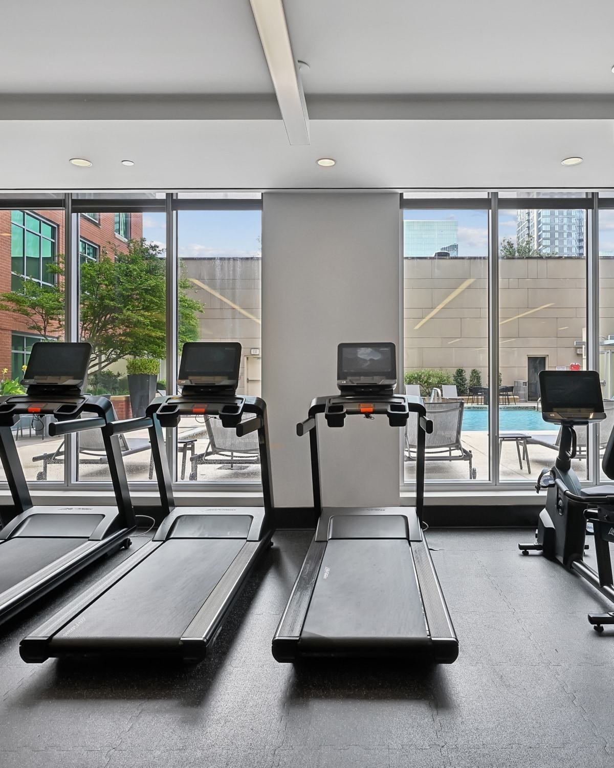 Apartment fitness center at Avant Reston featuring treadmills and exercise bikes facing large windows with pool views.