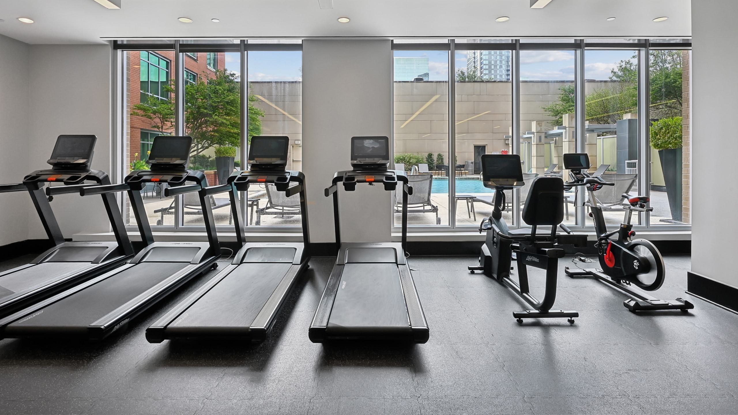 Apartment fitness center at Avant Reston featuring treadmills and exercise bikes facing large windows with pool views.