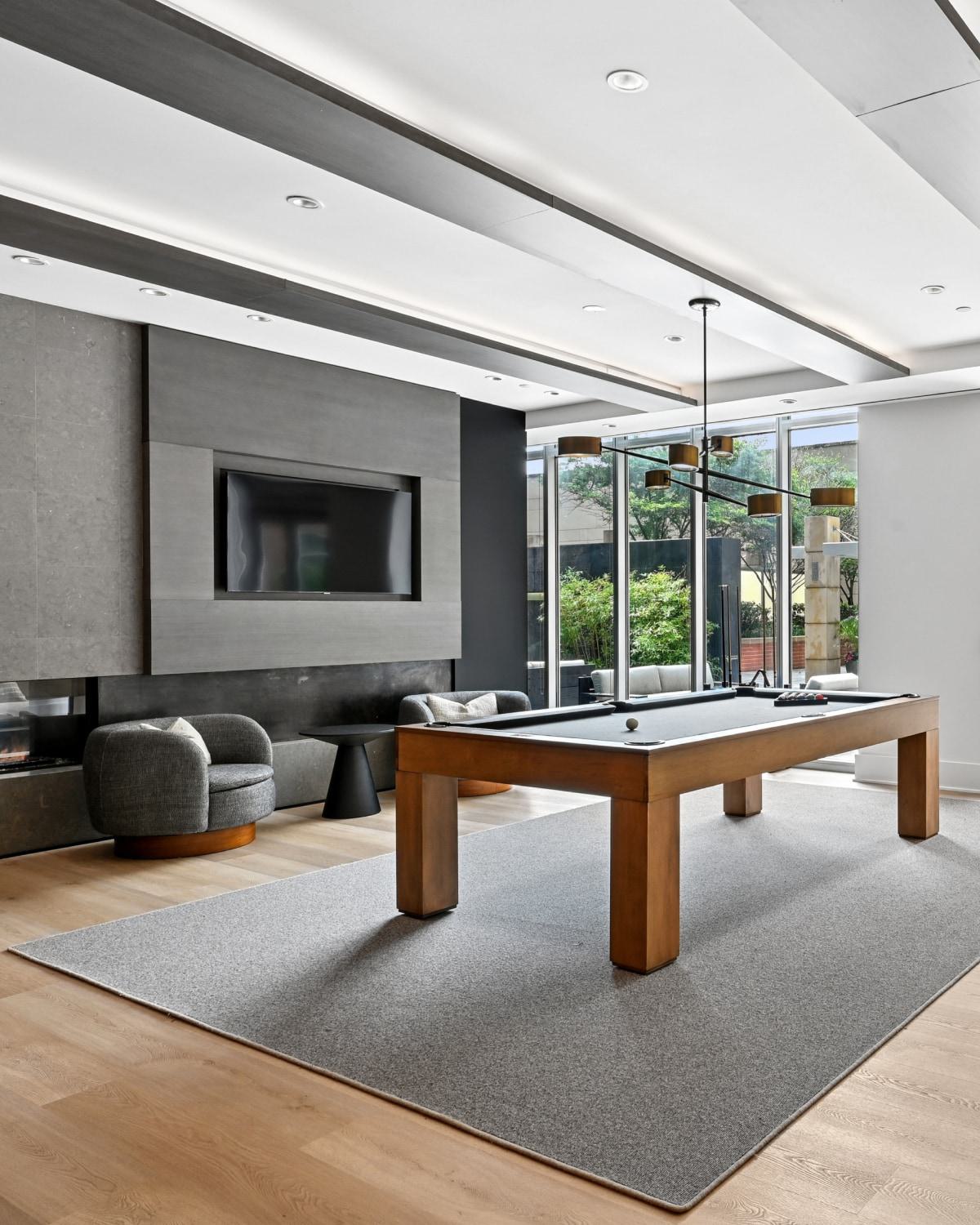 Resident game room at Avant Reston featuring a wooden pool table, shuffleboard table, fireplace, and patio access.