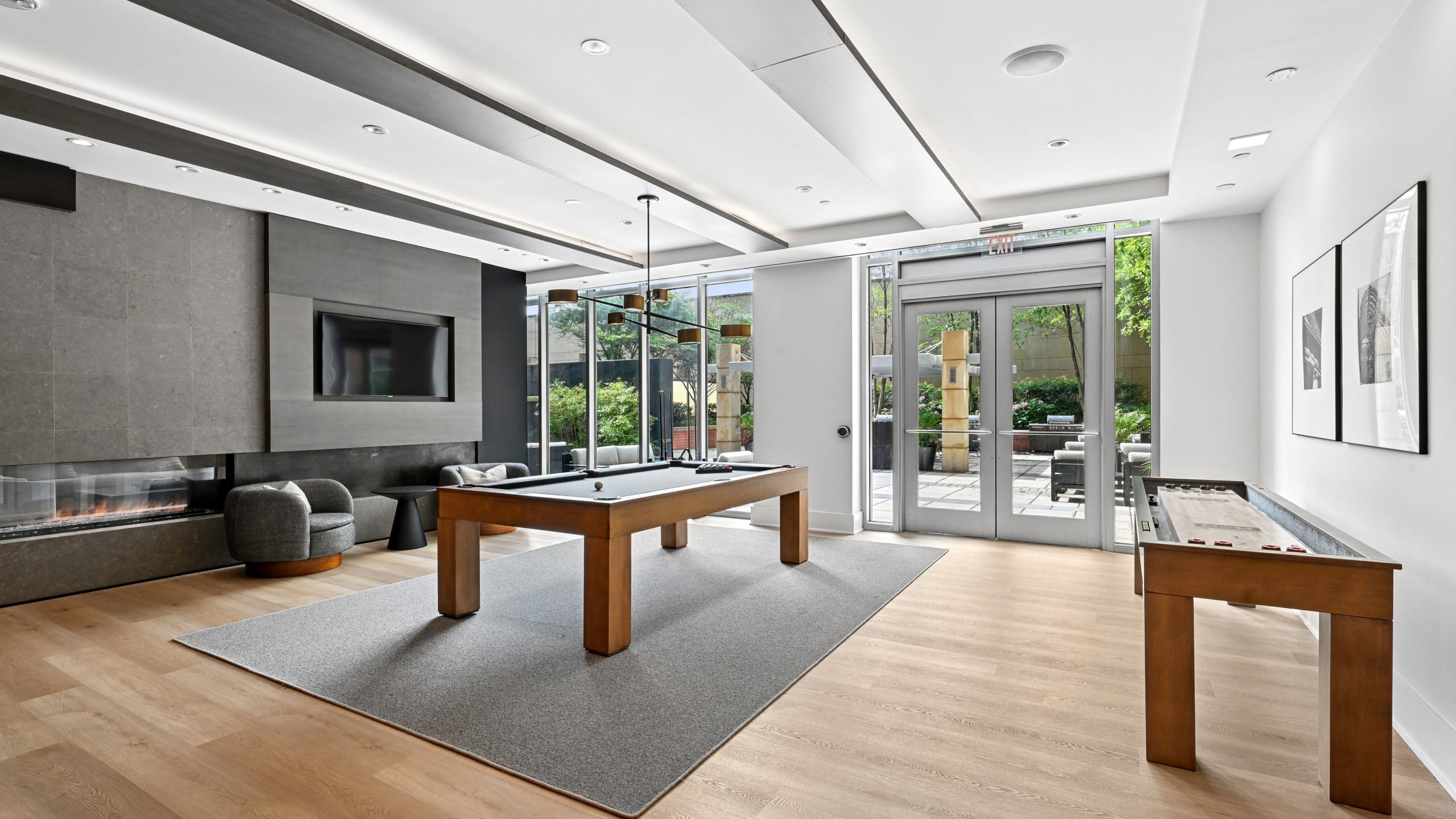 Resident game room at Avant Reston featuring a wooden pool table, shuffleboard table, fireplace, and patio access.