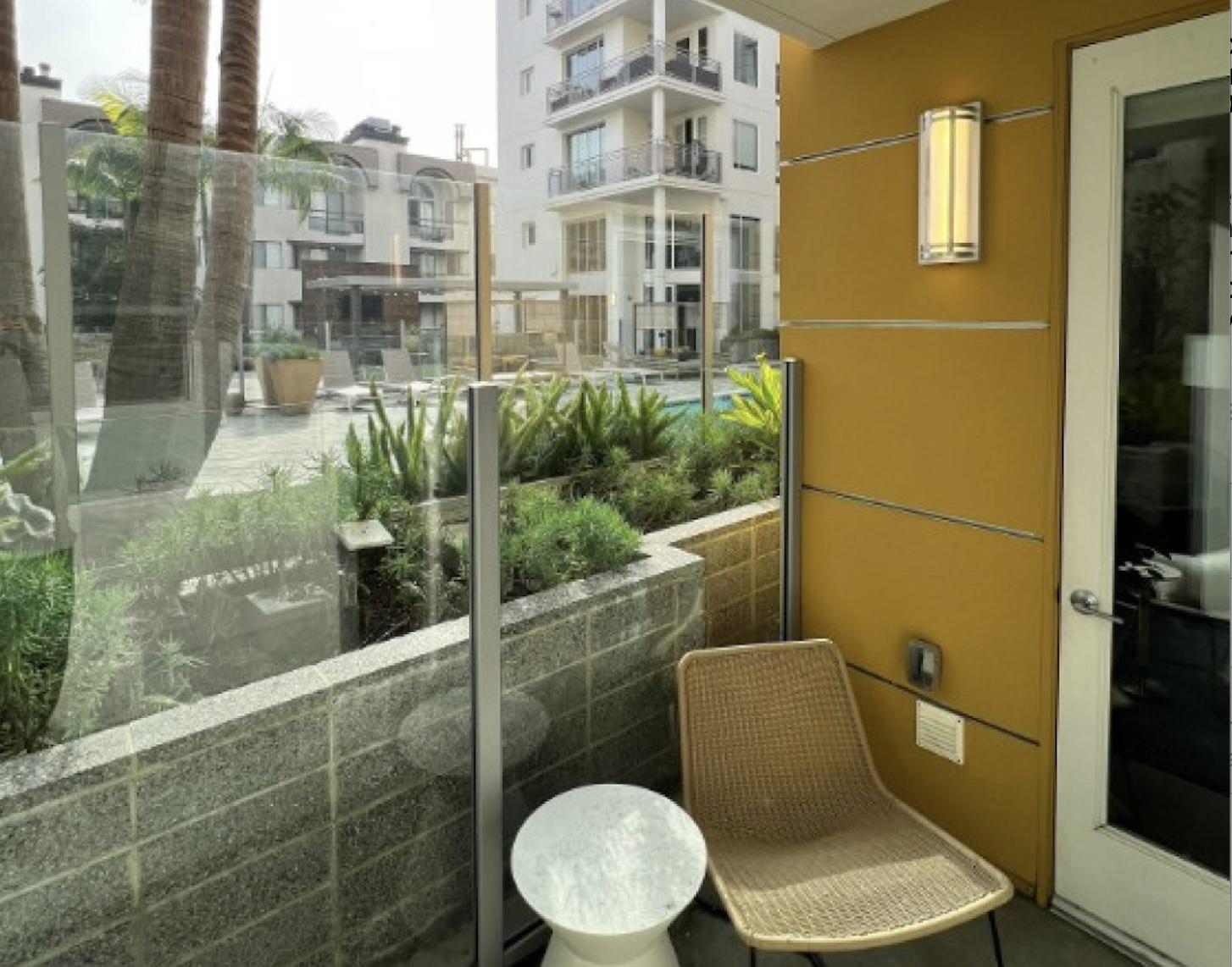 A ground-level private patio at Desmond featuring modern outdoor seating and a marble side table, separated from the central pool courtyard by a sleek glass and stone partition.