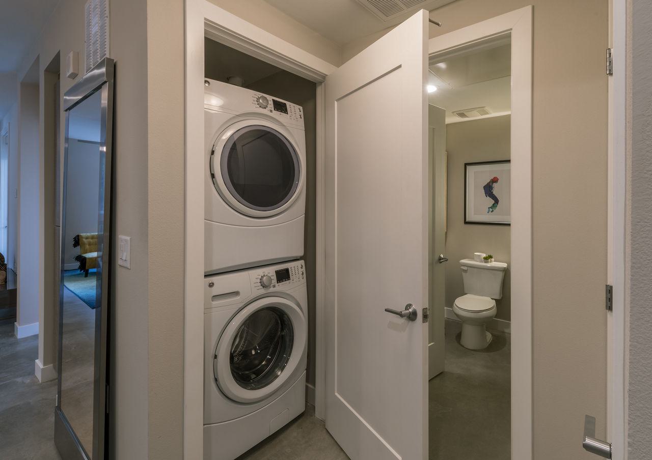 A modern apartment hallway featuring a stacked, white GE front-loading washer and dryer set integrated into a dedicated closet space next to a bathroom.