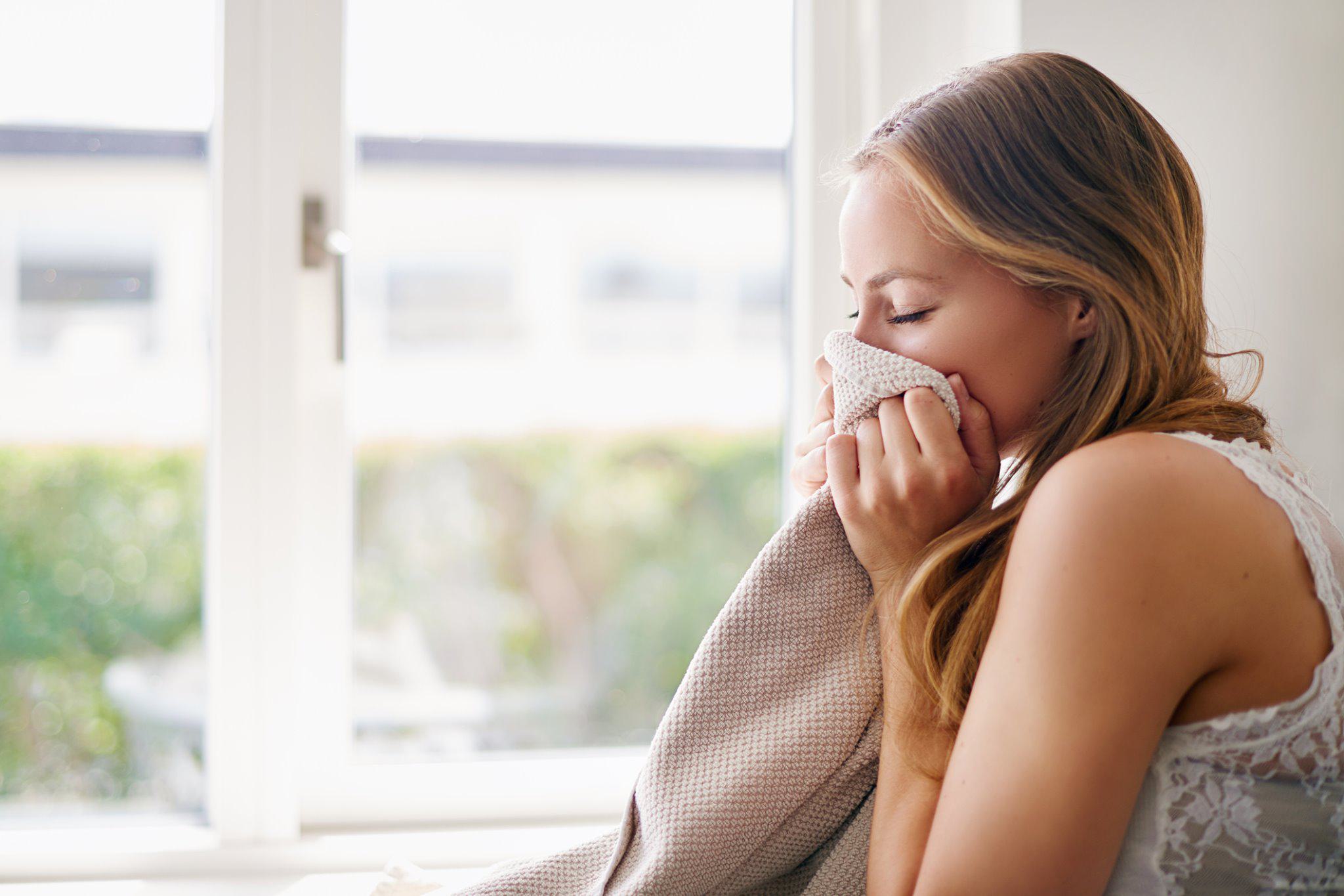 a woman by a sunny oversized window, folding laundry and enjoying the clean smell of a soft, freshly washed towel