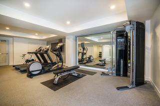 Brightly lit apartment fitness center showing a row of treadmills, an elliptical, a spin bike, and a cable machine.