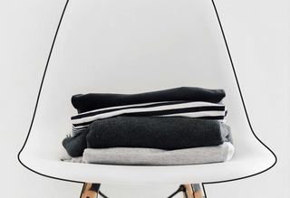 A neat stack of folded laundry sitting on a modern white chair with wooden legs.