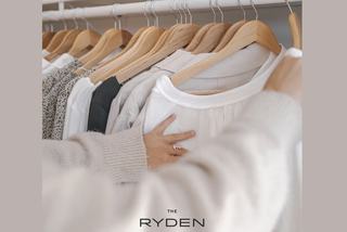 Close up of a person browsing through clothes hanging on wooden hangers inside a walk-in closet at The Ryden