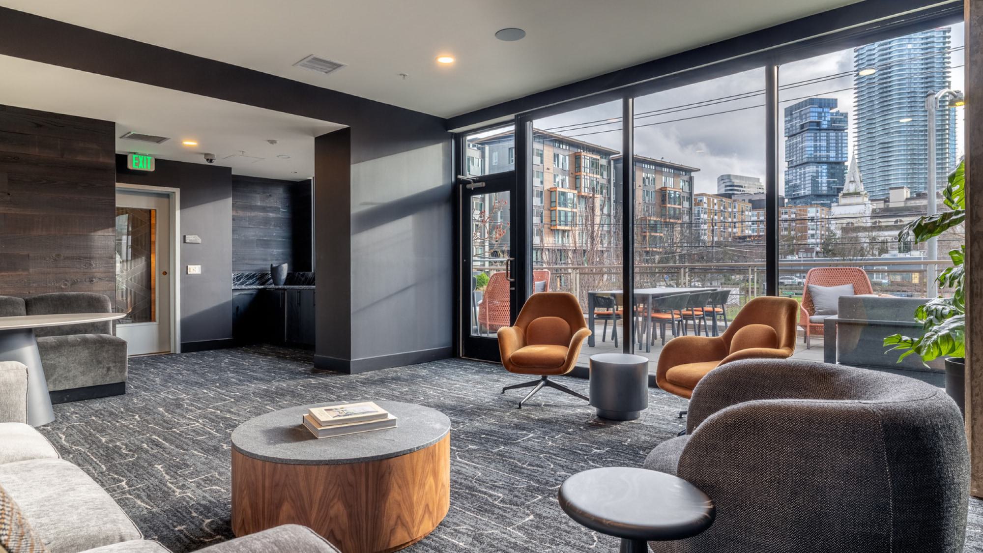 Modern resident lounge with floor-to-ceiling glass windows and doors opening to an outdoor city-view terrace.