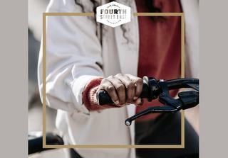 Close-up of a person's hand gripping a bicycle handlebar and brake lever, featuring a "Fourth Street East Jack London Oakland, CA" logo overlay