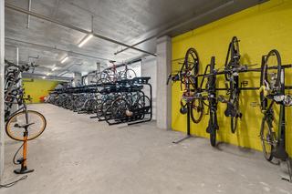 Secure indoor apartment bicycle storage room featuring concrete flooring, a bright yellow accent wall with vertical hanging racks, and black two-tier horizontal bike racks.