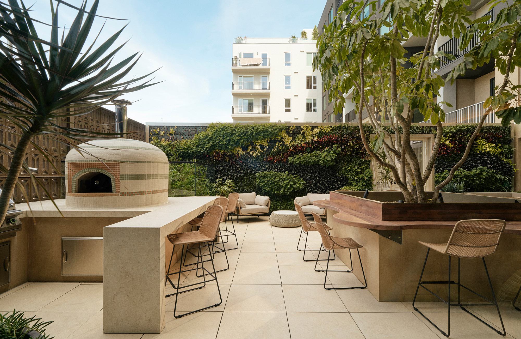 Outdoor kitchen at Rowyn featuring a dome wood-fired pizza oven, concrete counter with barstools, and a green living wall terrace.