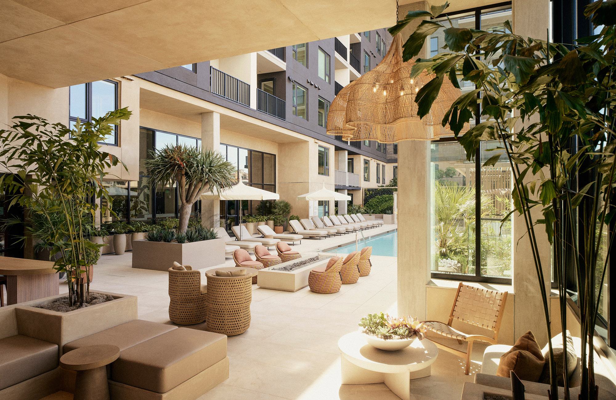 Resort-style pool courtyard at Rowyn with cushioned lounge chairs, a modern fire pit, and tropical palm trees under a shaded canopy.