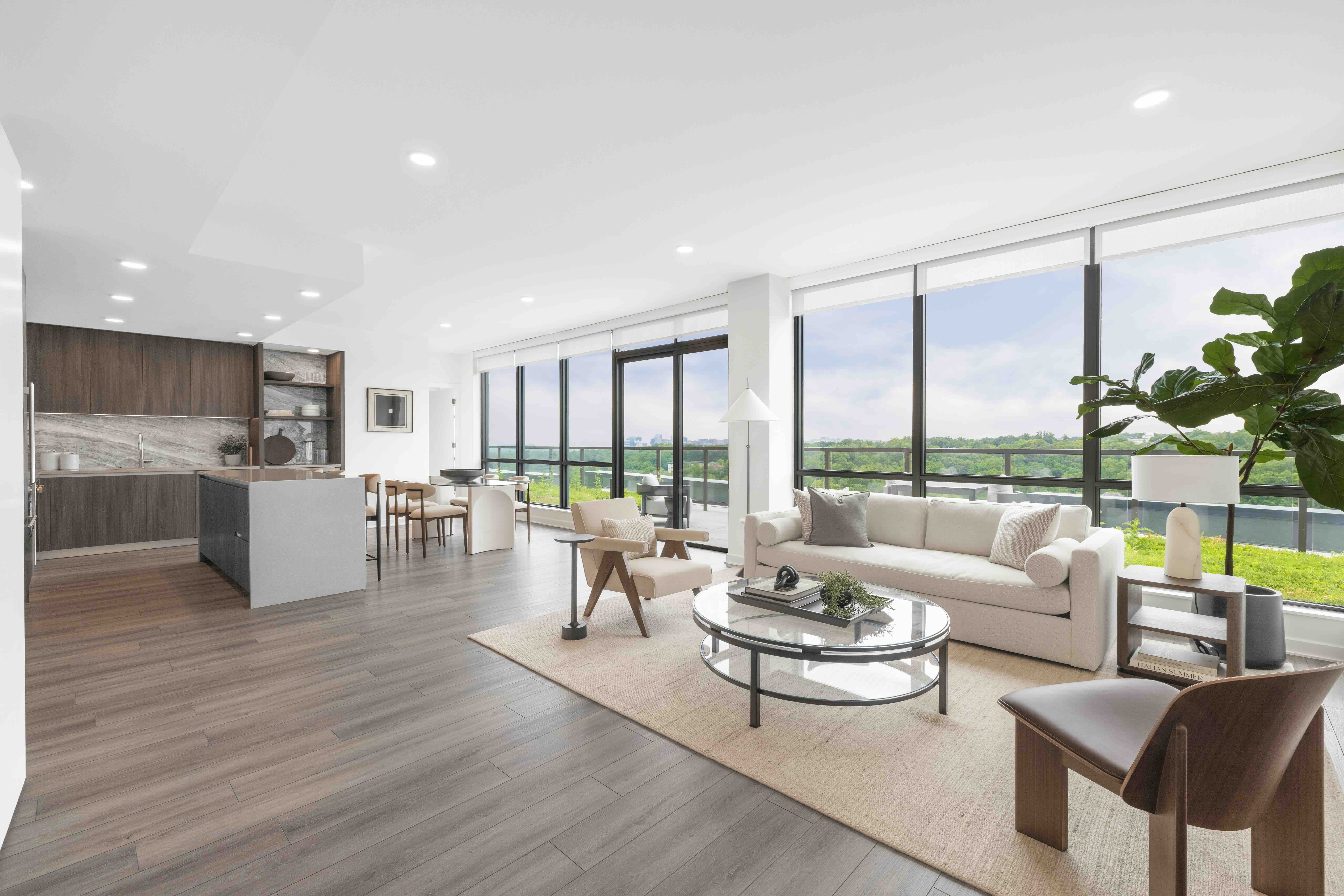 A bright penthouse living room with floor-to-ceiling sliding glass doors that open completely to a large, stone-paved outdoor terrace under a deep architectural overhang.