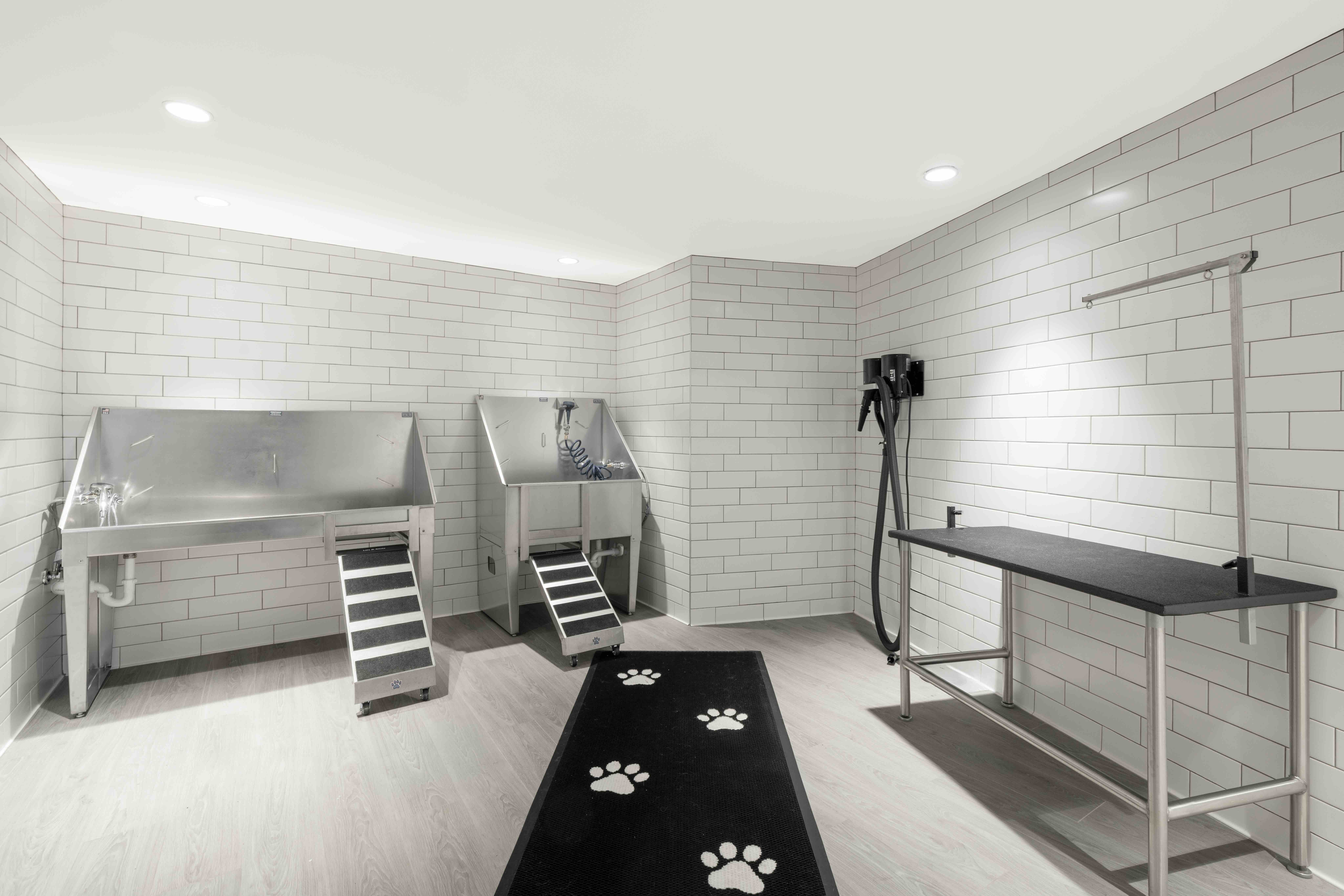 A professional residential pet spa with stainless steel washing tubs, a grooming table, and white subway tile walls.
