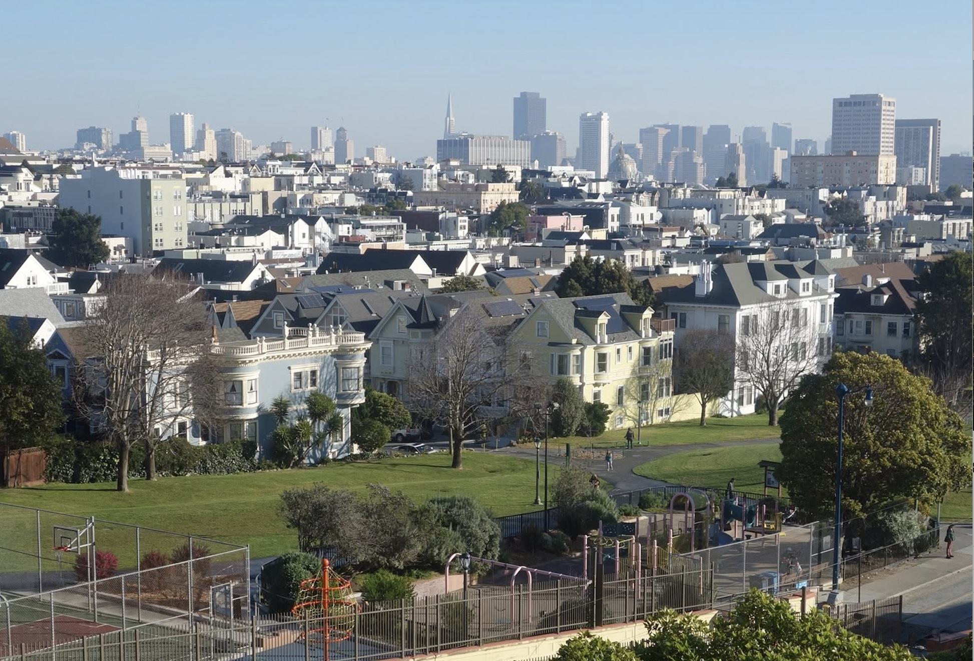 view of duboce park green spaces and paths with San Francisco skyline in the distance