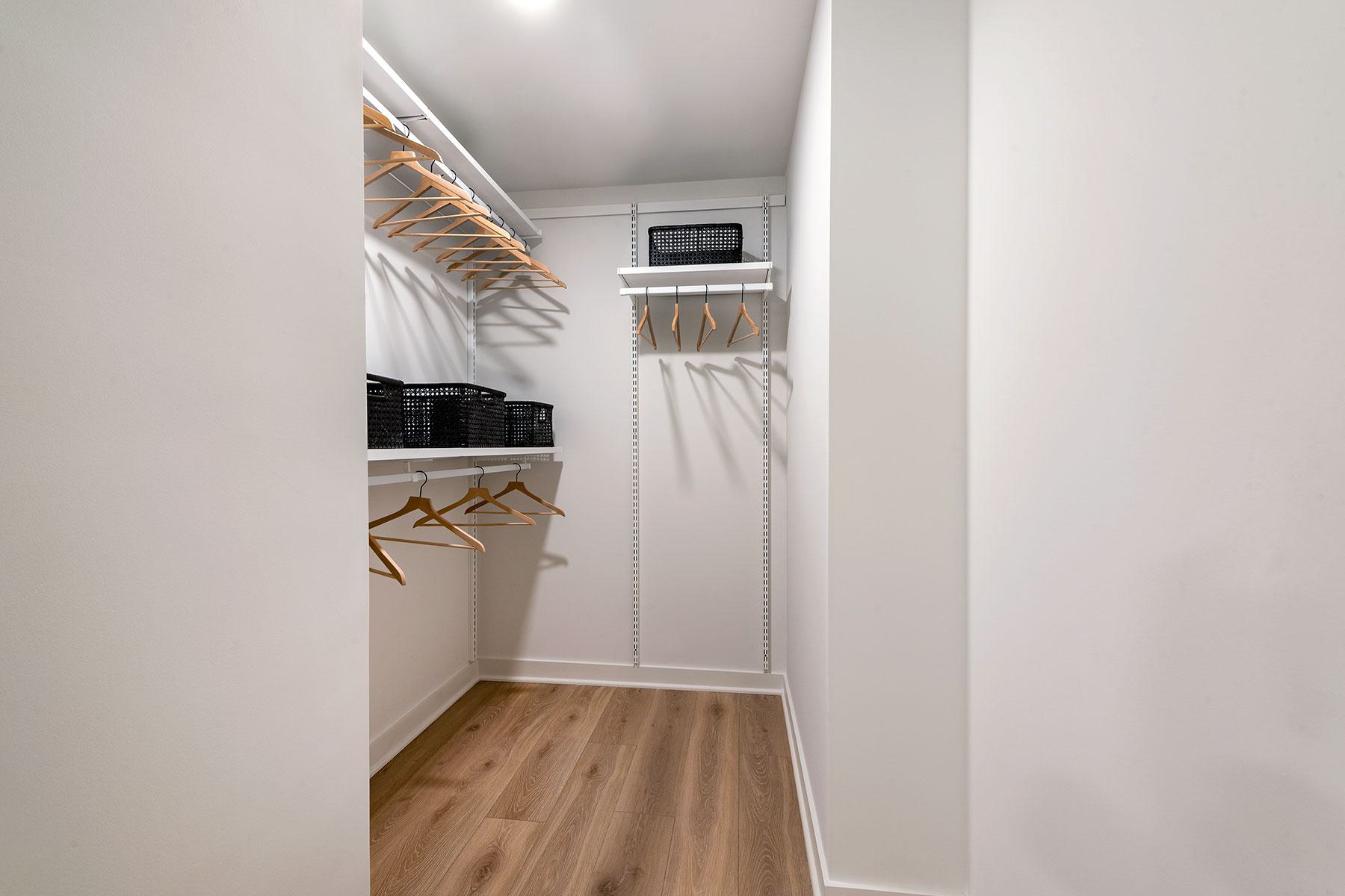 Spacious, modern walk-in closet with hardwood-style floors, white walls, and built-in adjustable shelving and clothing racks