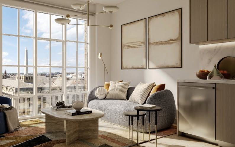 A modern apartment interior featuring a curved grey sofa, abstract wall art, and large multi-pane windows framing a direct view of the Washington Monument in the distance.