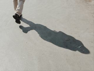a person wearing pants and sneakers walking on hard pavement with a shadow reflected