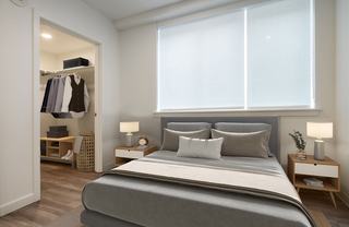 A modern bedroom featuring a large bed with grey linens and an open doorway revealing a spacious, organized walk-in closet at The Victor apartments.