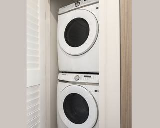 A modern, white Electrolux stacked washer and dryer set tucked into an apartment closet.
