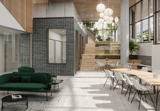 Bright, multi-level co-working lounge with high wood ceilings, a mezzanine staircase, shared work tables, and floor-to-ceiling windows.