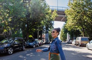 A woman in a denim jacket walks down a tree-lined street in Fremont, Seattle, with the George Washington Memorial Bridge (Aurora Bridge) visible overhead.