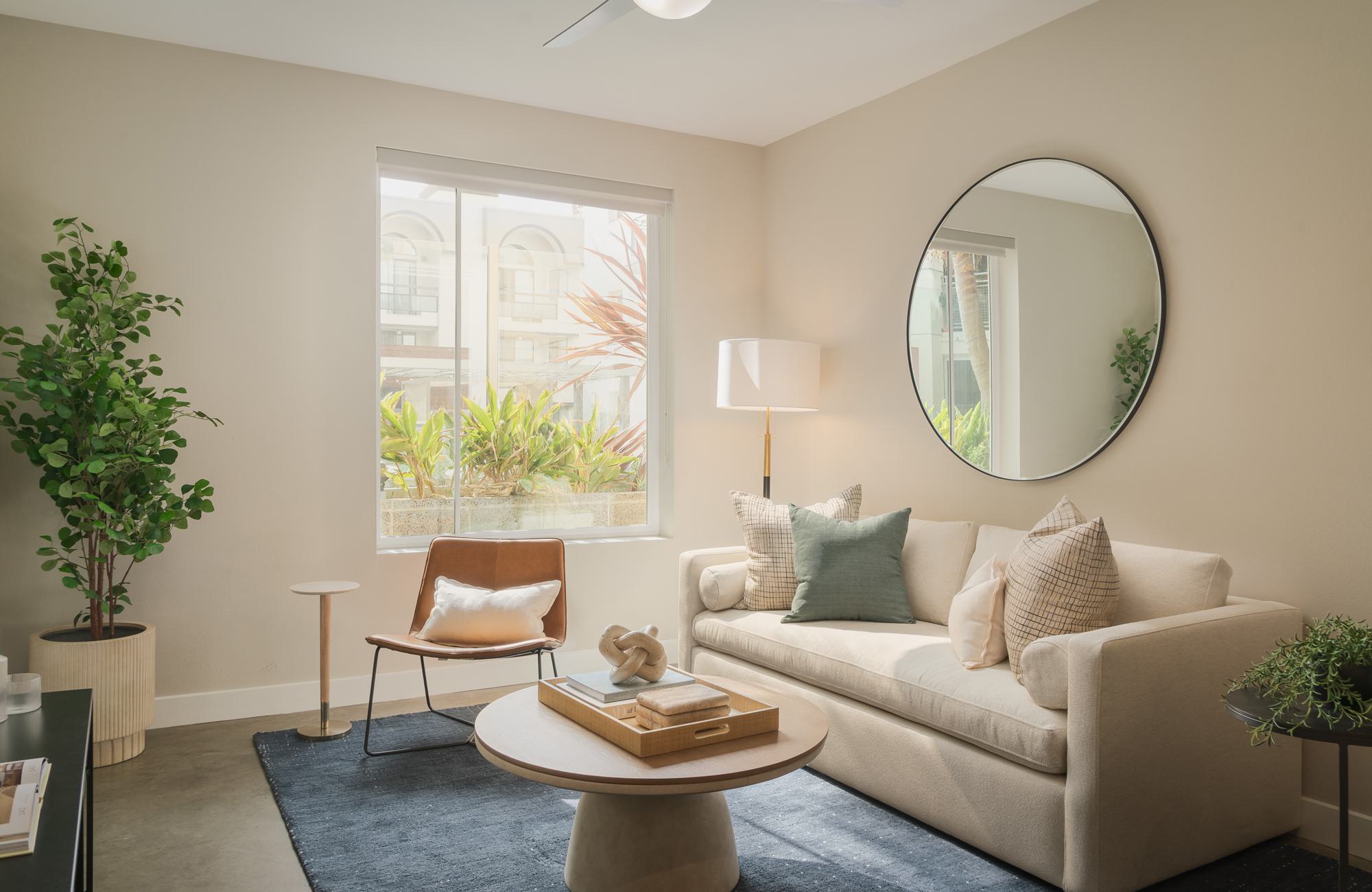 Modern apartment living room at The Desmond with cream sofa, round mirror, and large window