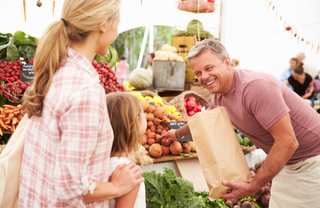 A family filling a paper bag with golden beats and other veggies at the farmers market