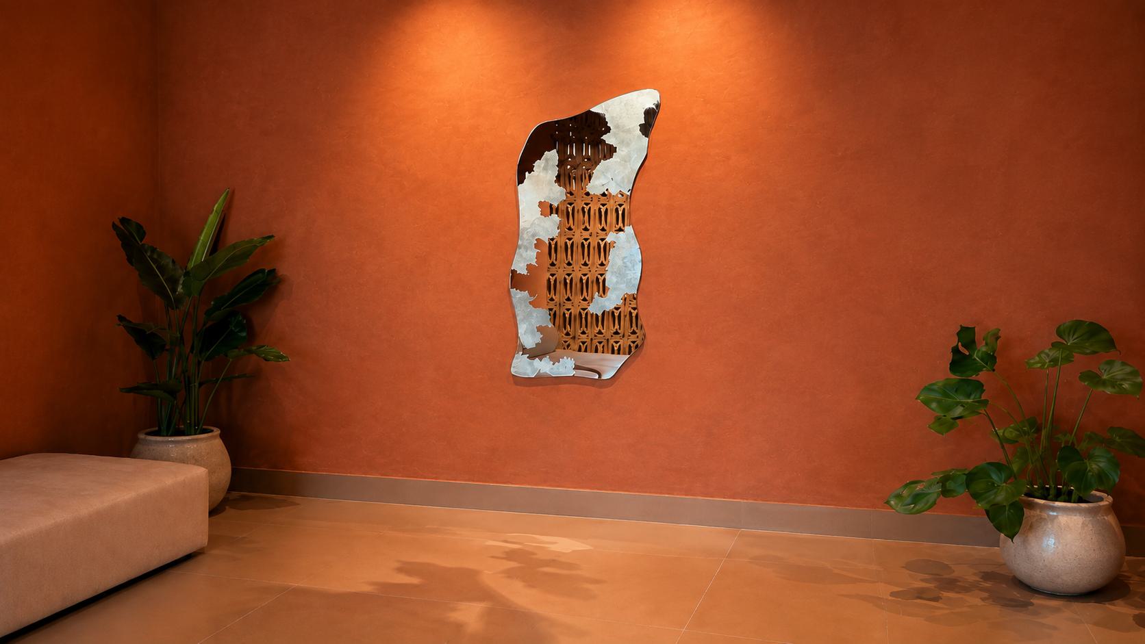 Irregular sculptural mirror with distressed silver detailing mounted on a warm terracotta wall.