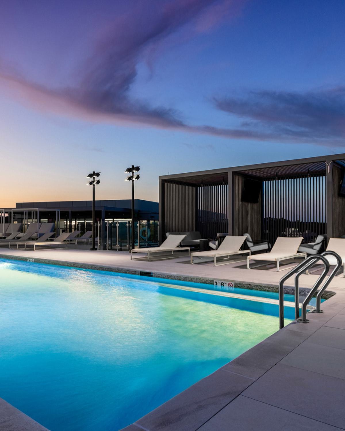 A rooftop pool lit with blue lights, with a purple sunset in the background.