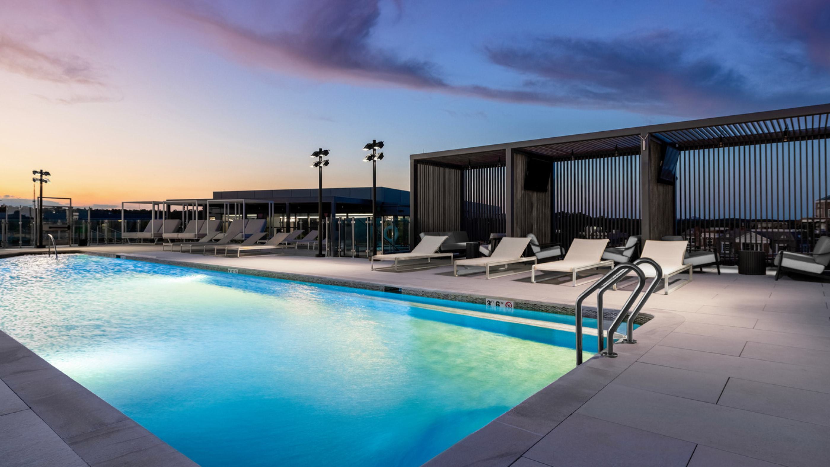 A rooftop pool lit with blue lights, with a purple sunset in the background.