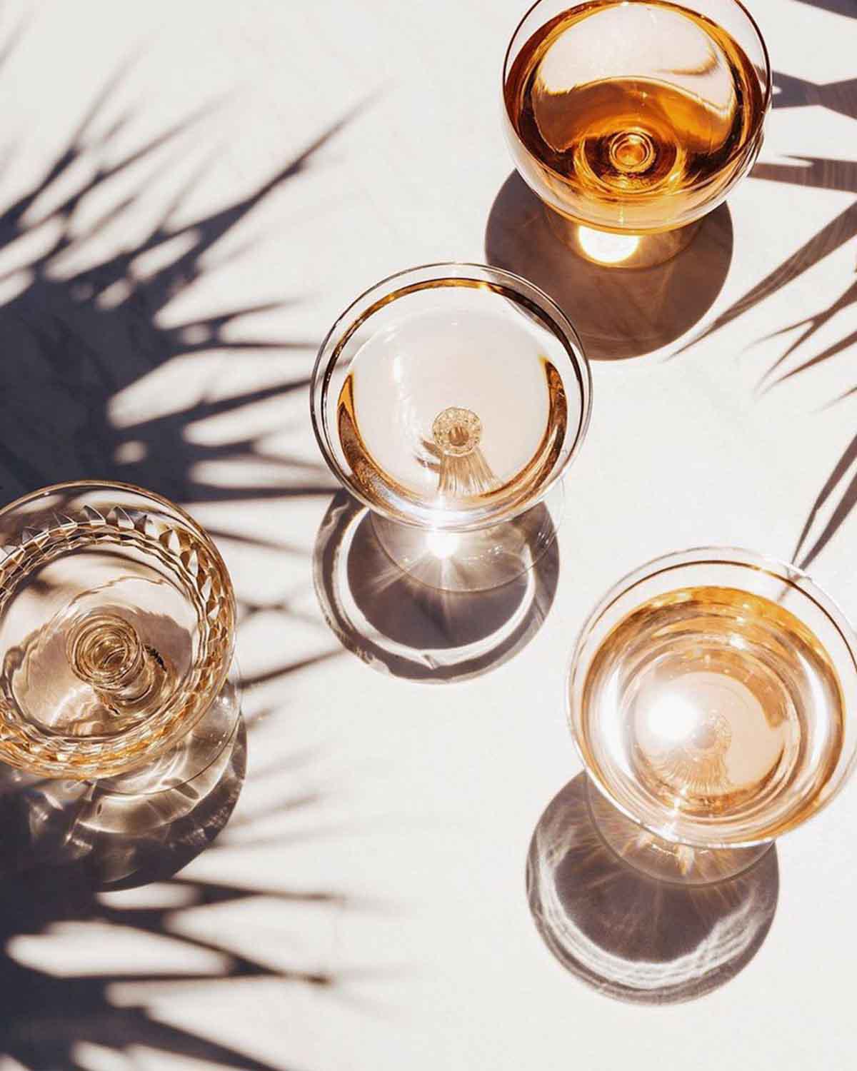 top-down view of cocktail glasses with golden drinks under sunny palm tree shadows.