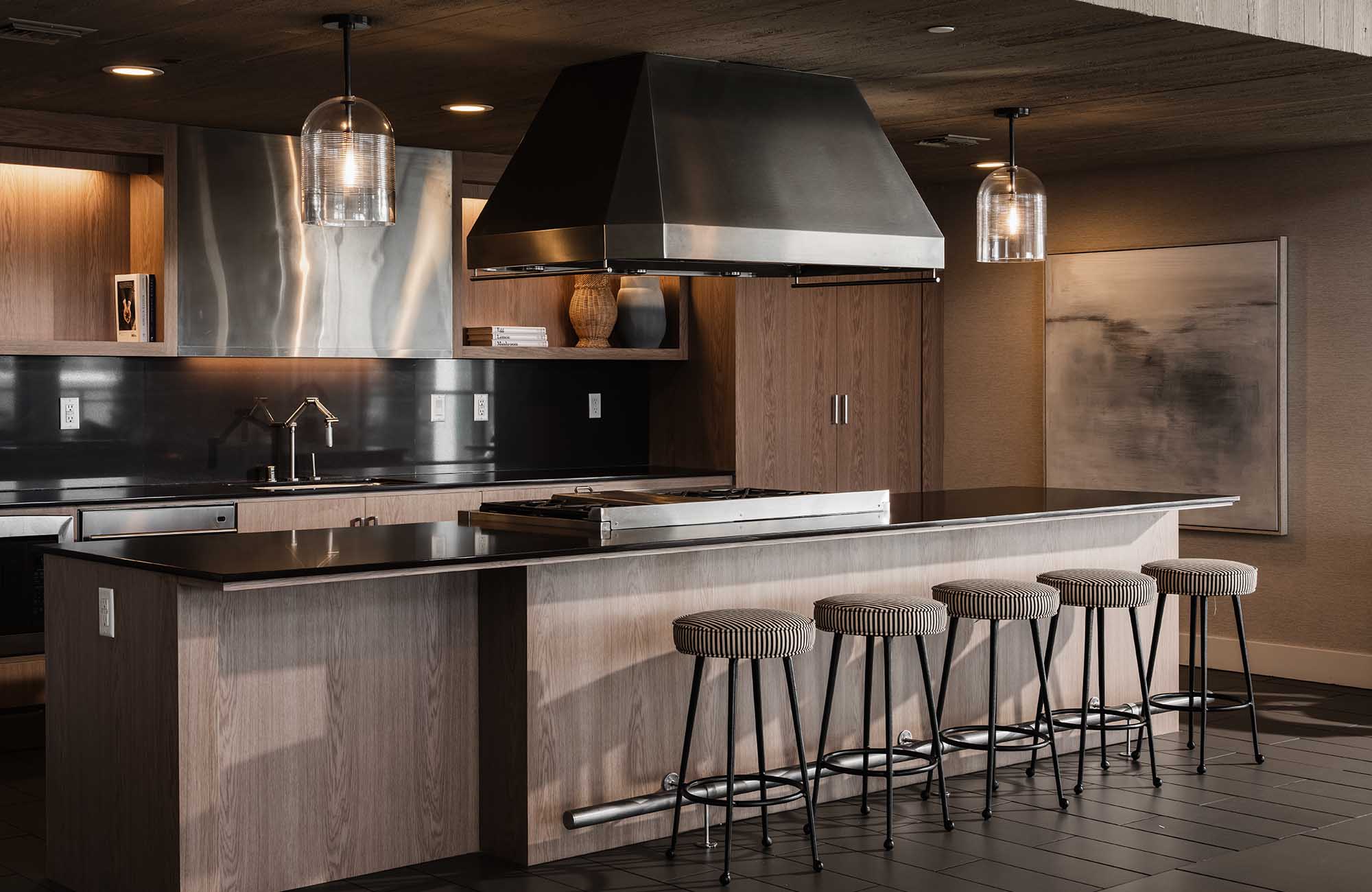 Luxury catering kitchen with large wooden island, bar stools, stainless steel range hood, and dark countertops.