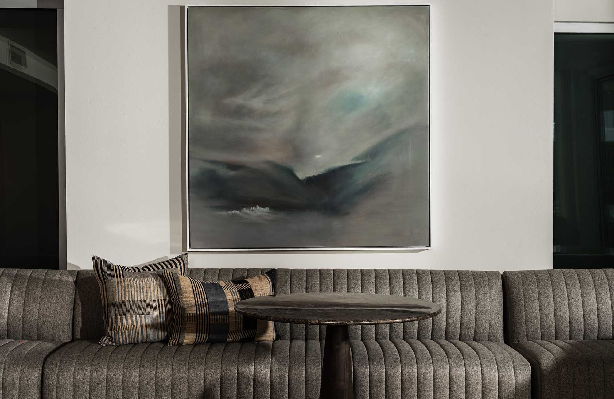Seating nook with channel-tufted sofa, dark wooden table, and large abstract wall art in modern apartment lounge.